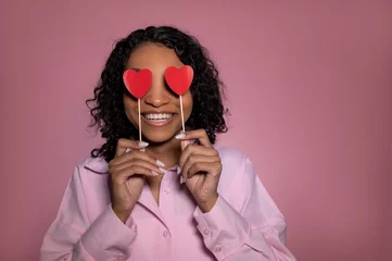 Fotobehang Happy african american girl blinded by big love. woman holding red heart-shaped cards over eyes and smiling,St valentines day concept © piksik