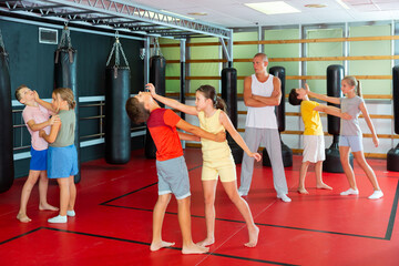 Preteen children practicing in pair self-defence movements with male trainer supervision