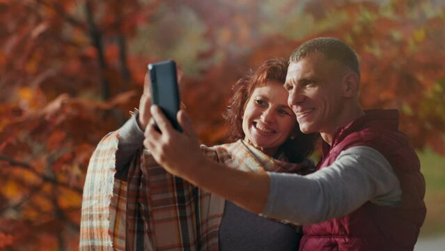 Hello autumn. happy romantic couple in the park using smartphone and taking selfie.