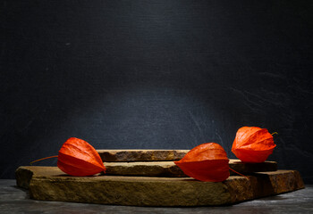 stones for the podium. stones on a dark background and orange physalis for product presentation, podium, background. medicine cosmetics perfumery concept. - obrazy, fototapety, plakaty