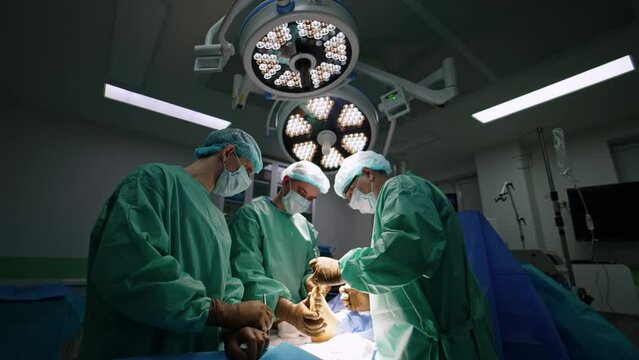 Three male surgeons work with foot of a patient. Doctors carefully operate the injured limb.