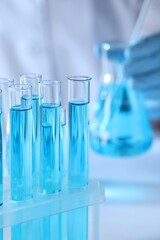 Scientist holding flask near test tubes with light blue liquid, selective focus