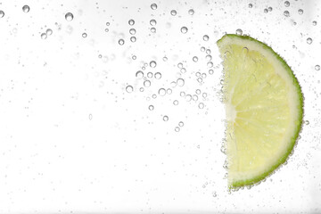 Juicy lime slice in soda water against white background, closeup. Space for text