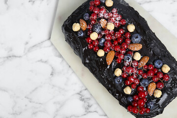 Delicious chocolate sponge cake with berries and nuts on white marble table, top view. Space for text