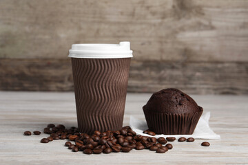 Paper cup with white lid, coffee beans and muffin on wooden table. Coffee to go
