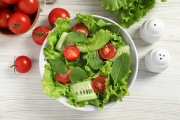 Delicious vegetable salad, cherry tomatoes, lettuce, pepper and shakers on white wooden table, flat lay