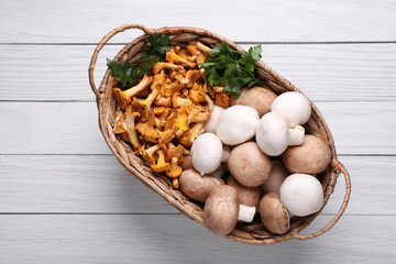 Basket with different mushrooms on white wooden table, top view