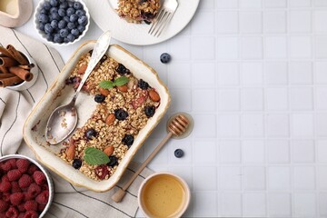 Tasty baked oatmeal with berries and almonds on white tiled table, flat lay. Space for text