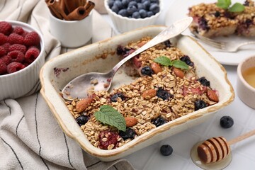 Tasty baked oatmeal with berries and almonds in baking tray on white table