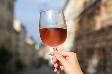 Woman holding glass of rose wine outdoors, closeup