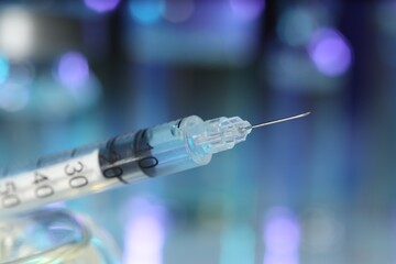 Syringe with medicine against blurred background, closeup