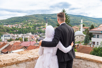 A Muslim couple stand on balcony and watch the cityscape.