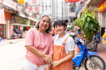 Happy Asian family grandmother and grandchild girl walking and shopping together at street market. Senior woman and little girl enjoy and fun outdoor lifestyle travel in the city on summer vacation.