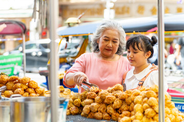 Asian family grandmother and grandchild girl buying and eating street food together at street...