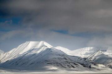 2022-05-09 SNOW CAPPED MOUNTAIN RANGE IN THE ARCTIC NEAR SVALBARD WITH STORMY CLOUDS MOVING IN