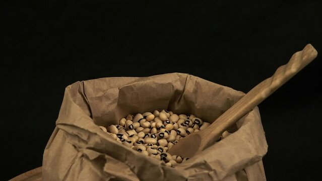 Wooden spoon in paper bag of dried black-eyed peas, isolated on black