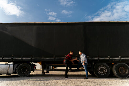 Father And Son Together Starting Trucking Business, Shaking Hands In Front Of Long Hail Truck With Trailer 