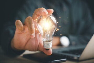 Businessman's hand holds a creative light bulb, representing a moment of inspiration. Showcases the concept of innovation, imagination, and successful profit in global business. - obrazy, fototapety, plakaty