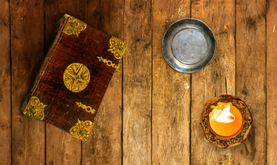 An old book with decorative cover with candle on an old table from planks