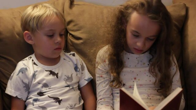 SISTER READING TO BROTHER FROM BOOK AT BEDTIME