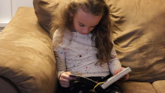 LITTLE GIRL READING A BOOK ALONE ON THE COUCH