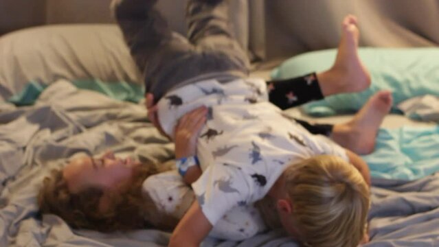 YOUNG SISTER AND BROTHER HAVING FUN WRESTLING ON BED