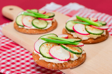 Light Breakfast or Diet Eating - Crispy Cracker Sandwich with Cream Cheese, Fresh Cucumber, Green Onions and Radish on Wooden Cooking Board on Magenta Background