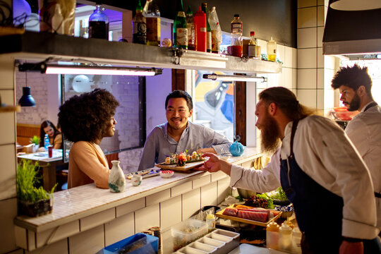 Young sushi chef serving sushi to a diverse couple in a sushi restaurant or bar