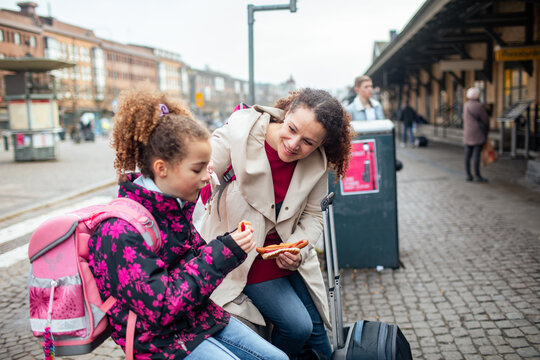 Young mixed mother and daughter having a snack while waiting for the arrival of their train at the train station