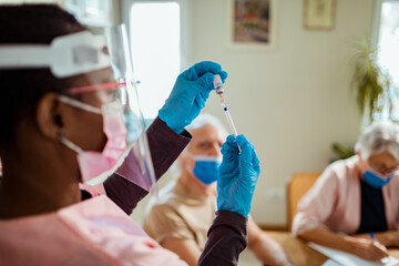 Young African American caregiver preparing a vaccine for her patient in their home