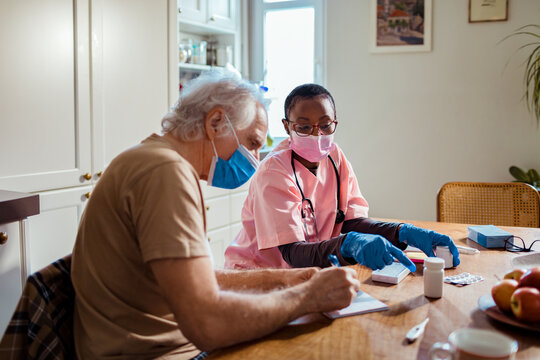 Young African American caregiver going over medication with her senior male patient at his home