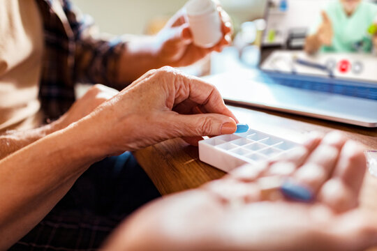 Senior Caucasian couple organizing their pills in a dosette box with advice from their doctor on a video call at home