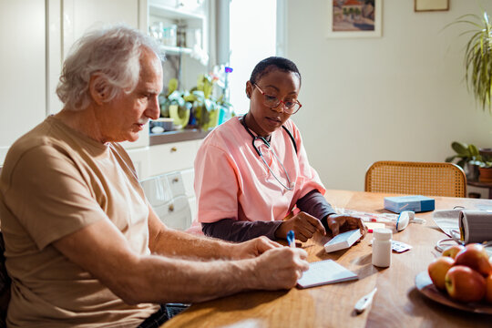 Young African American caregiver going over medication with her senior male patient at his home