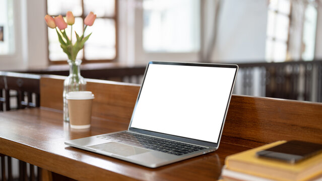 Close-up image of a white-screen laptop mockup on a wooden table in a minimalist coffee shop.