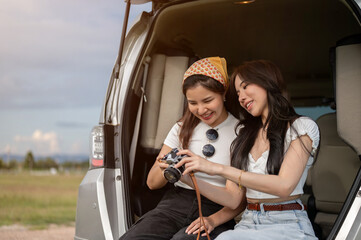 Two happy Asian female are checking the pictures on the camera, having fun during their road trip