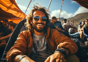 Obraz premium An attractive middle-aged man with a beard and wearing sunglasses sits near a tent while camping with friends