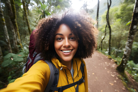 Happy traveller black woman with backpack taking selfie picture in forest- Travel blogger taking self portrait with smart mobile phone device outside - Life style and technology concept