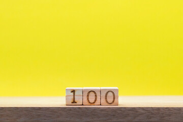 机の上に100の数字のウッドキューブが中央に並んだ黄色い背景の正面