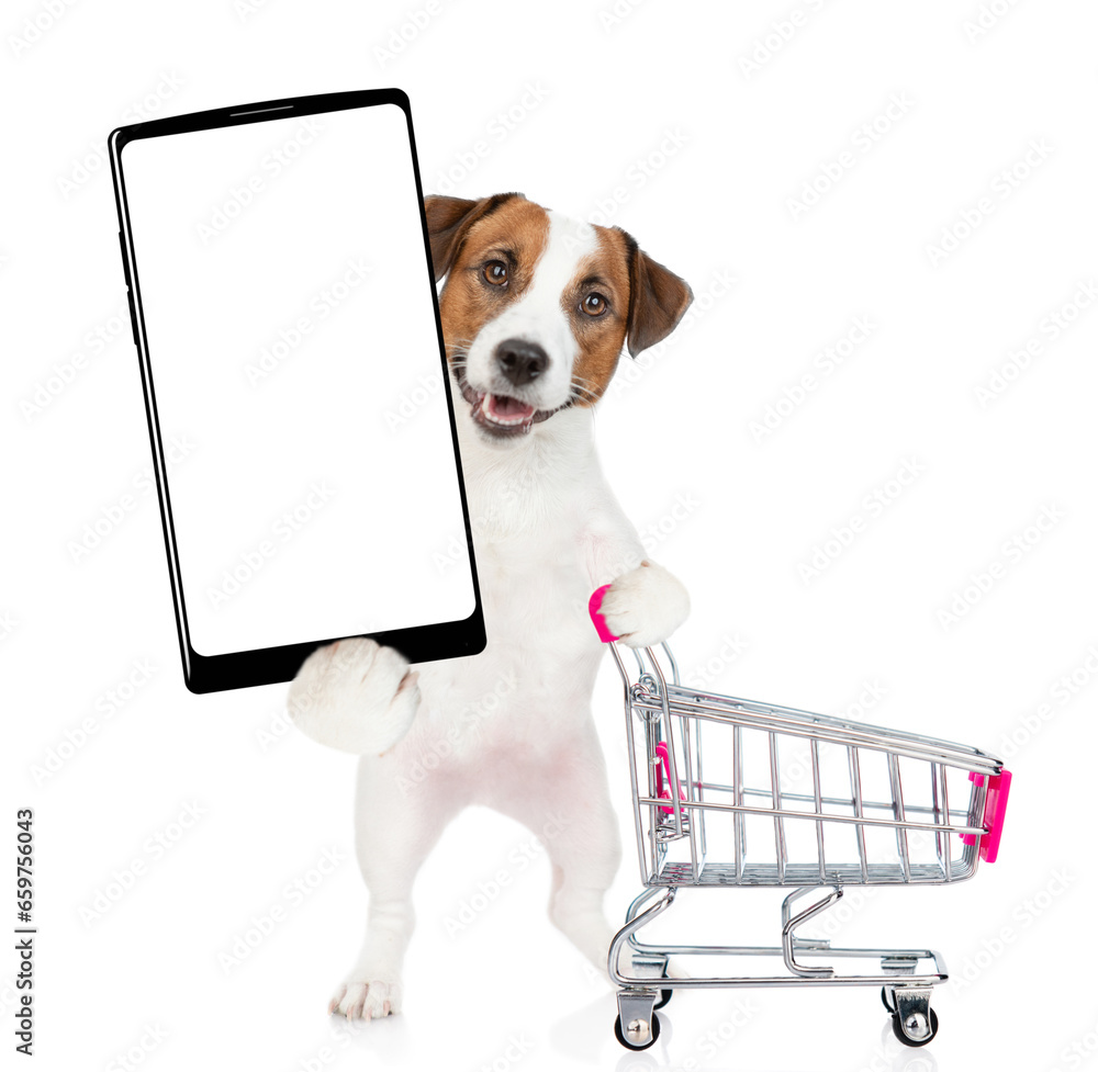 Poster jack russell terrier puppy pushing a shopping cart and holds big smartphone with white blank screen 