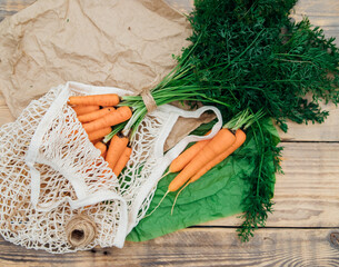 Eco-friendly mesh shopping bag with freshly picked carrots, on a wooden background.Zero waste, plastic free concept . Healthy food, freshly squeezed juice.