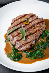 steak in gravy with herbs on it on a white plate