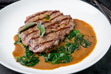 steak in gravy with herbs on it on a white plate