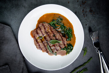 steak in gravy with herbs on it on a white plate