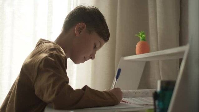 School kid boy studying lesson writing with pen at home. Primary class pupil write homework