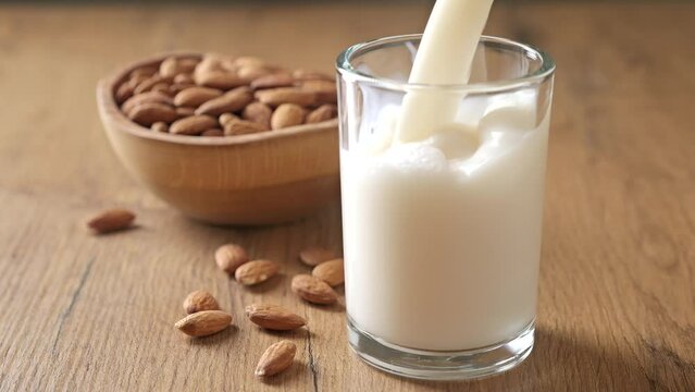 Close-up of pouring almond milk into a glass. Vegan lactose free milk. Plant based milk and almonds.