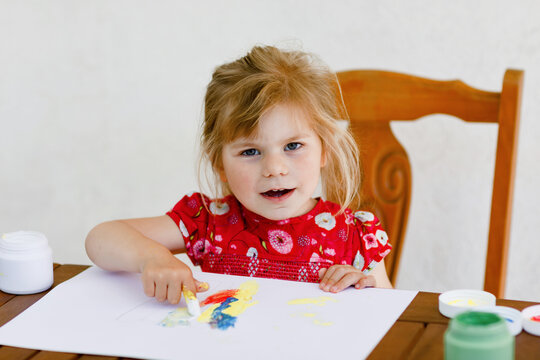 Little creative toddler girl painting with finger colors a fish. Active child having fun with drawing at home, in kindergaten or preschool. Education and distance learning for kids. Creaitve activity.