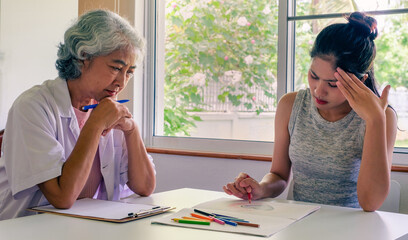 Psychologist session. A middle aged woman in therapy with a senior woman psychologist. Psychiatrist studies and examines patient with drawings and gestures. Psychotherapy concept. 