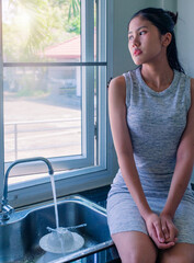 Young woman depressing of her work and life sitting alone by the window and lookin out and letting water flowing. Worried some concept. 