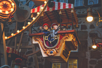 Little preschool girl and school boy riding on ferris wheel carousel horse at Christmas funfair or market, outdoors. Two happy children having fun on traditional family xmas market in Germany