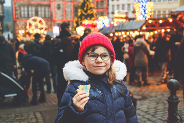 Little cute preschool girl eating gingerbread cookie on German Christmas market. Happy child on...